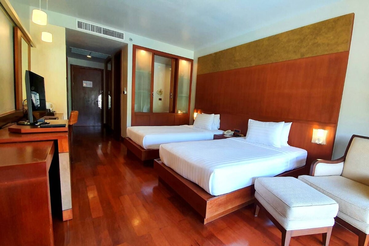 A hotel room with two beds, a desk, a chair, and a television.