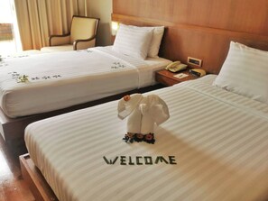Two hotel beds with "WELCOME" spelled out on the bedspread, a bedside telephone, and a chair in the background. - Mission Hills Phuket Golf Resort & Spa (Wichit)
