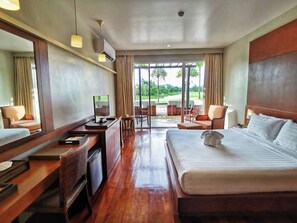 Camera d'albergo con un letto grande, una scrivania con un computer, una sedia e vista su un giardino attraverso ampie finestre.