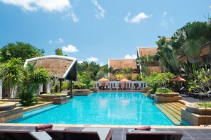 Una piscina con sillas de descanso y macetas, rodeada de edificios y vegetación.