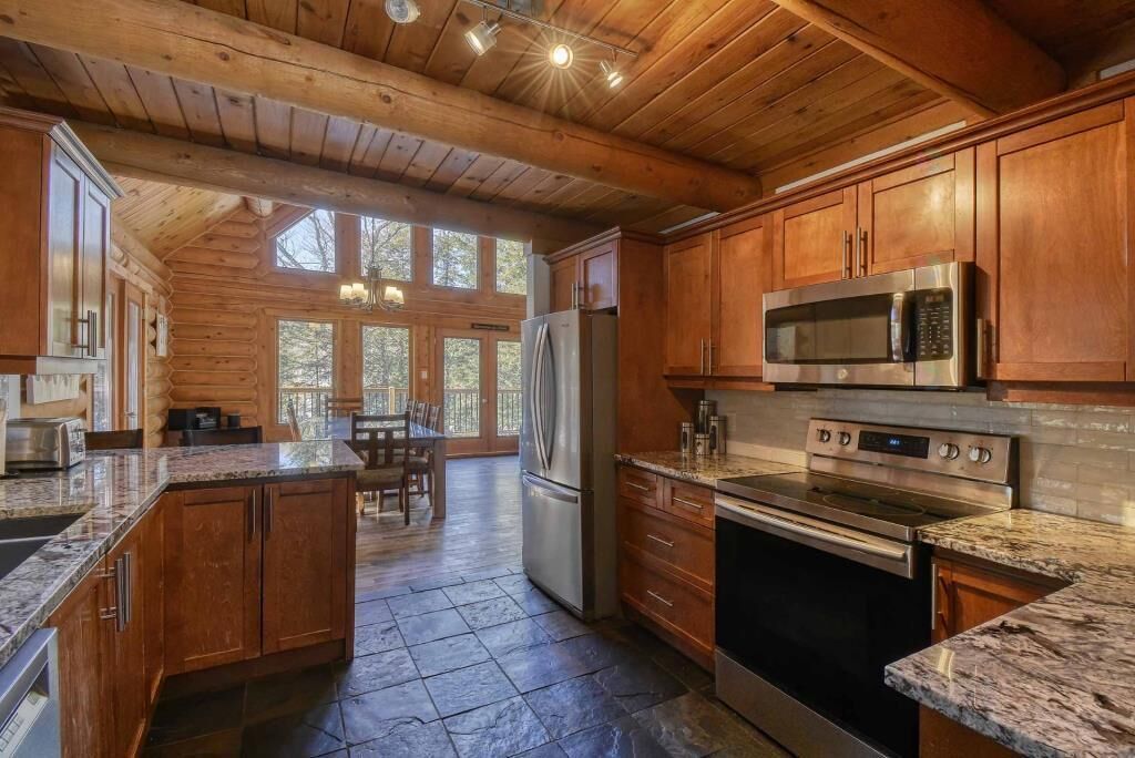 Cocina tipo cabaña de madera con encimeras de granito, electrodomésticos de acero inoxidable y piso de piedra.