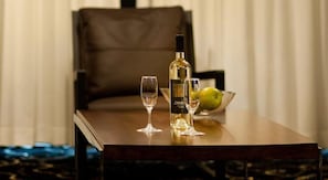 Une table avec une bouteille et deux verres, un saladier de fruits et une chaise à l’arrière-plan.