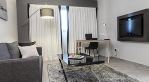 Uma sala de estar moderna com sofá, mesa de centro de vidro, escrivaninha com computador e televisão na parede.