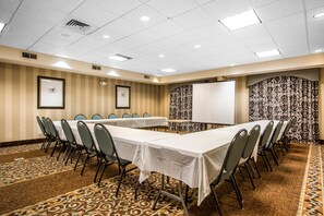 Une salle de conférence avec de longues tables, des chaises, un tableau blanc et des rideaux à motifs.
