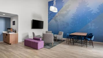 Una sala moderna con un televisor de pantalla plana, una mesa de comedor de madera con sillas, un sofá púrpura y un sillón gris.