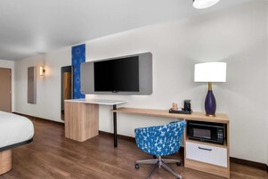 Habitación de hotel con cama, escritorio con televisor de pantalla plana, silla, lámpara y microondas.