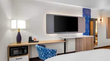 A hotel room with a bed, a desk with a lamp, a microwave, a flat-screen TV, and a mirror.