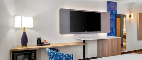 Habitación de hotel con cama, escritorio con lámpara, microondas, televisión de pantalla plana y espejo.
