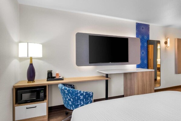 A hotel room with a bed, a desk with a lamp, a microwave, a flat-screen TV, and a mirror. - Spark by Hilton Pelham Birmingham I 65 (Pelham)