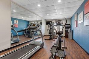 A gym with exercise equipment, a mirrored wall, and a blue wall with motivational posters. - Spark by Hilton Pelham Birmingham I 65 (Pelham)