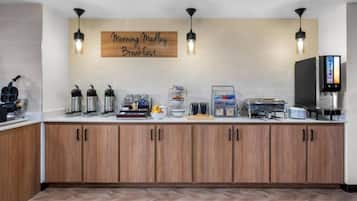 Un área de desayuno con un letrero que dice 'Morning Mellow Breakfast', equipada con cafeteras, un bol de frutas y un dispensador de agua.