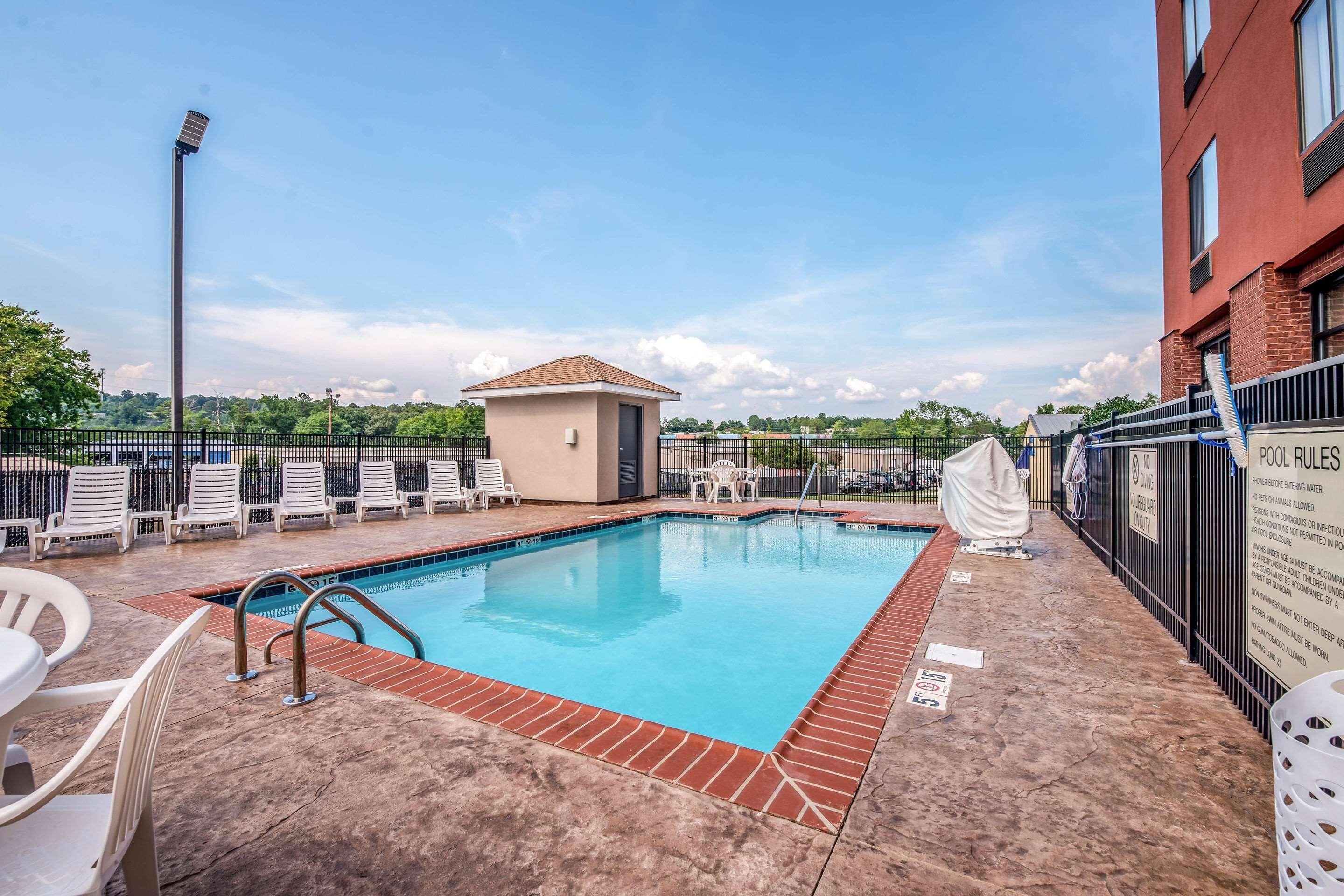 A swimming pool with a brick border, lounge chairs, a small building, and a fence.