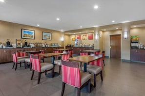 Ein Hotel-Speisesaal mit mehreren Tischen und Stühlen, einem Küchenbereich mit Geräten und gerahmten Bildern an den Wänden.