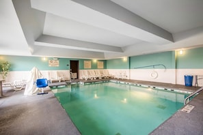 Ein Hallenbad mit glasklarer Wasseroberfläche, Sprungbrett und Liegestühlen an der Wand.