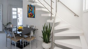 Et moderne interiør med en spiraltrappe, et spiseområde med et glasbord, stole og en potteplante.