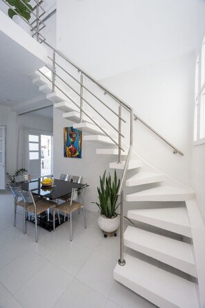 Ein modernes Interieur mit einer Wendeltreppe, einem Essbereich mit Glastisch, Stühlen und einem Blumentopf.