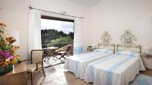 A bedroom with two beds, a balcony, a chair, and a table. - Parco Degli Ulivi (Arzachena)