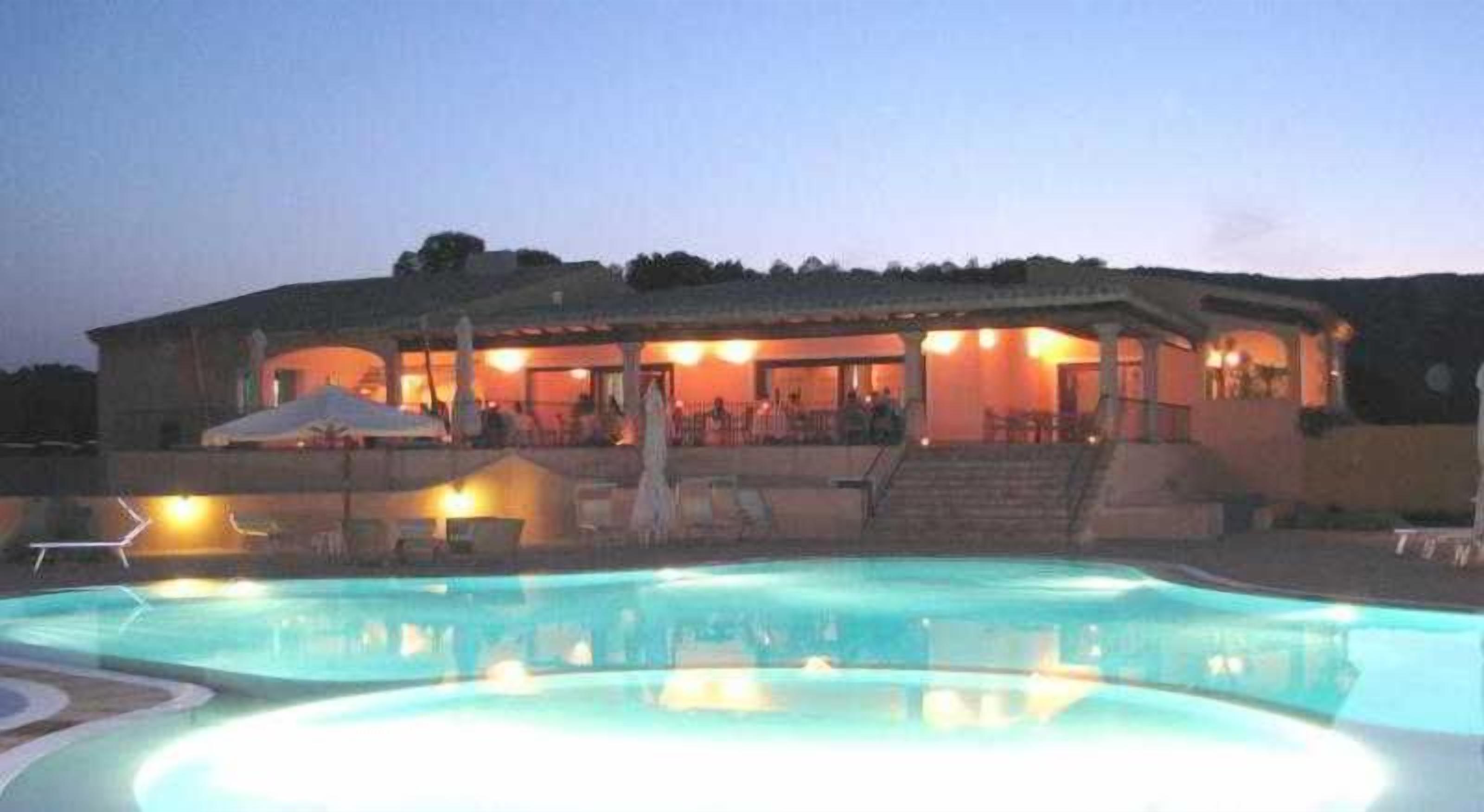 A building with a swimming pool, outdoor seating, and a covered area with stairs leading up to it.