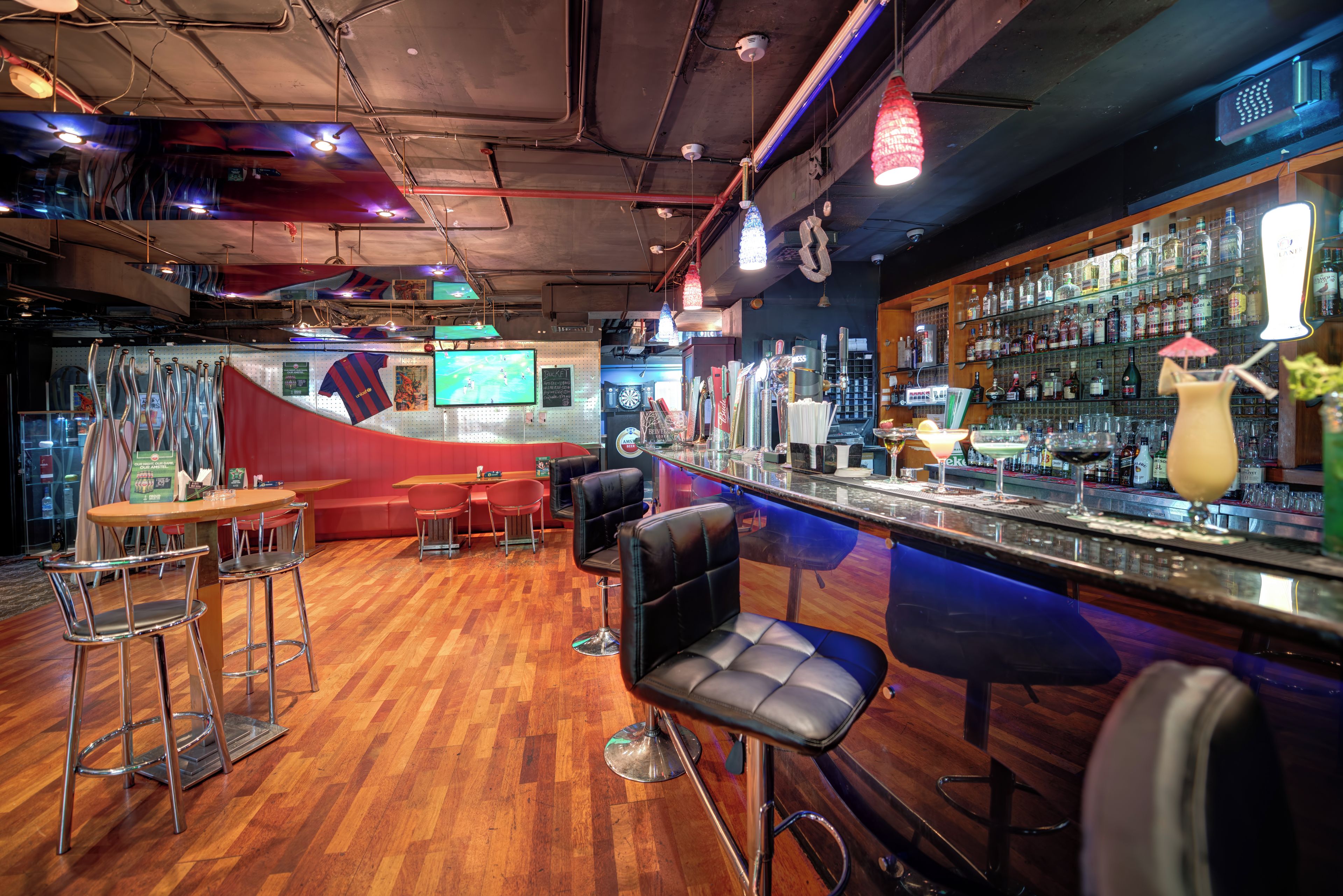A bar area with stools, a counter with bottles, and a red couch.