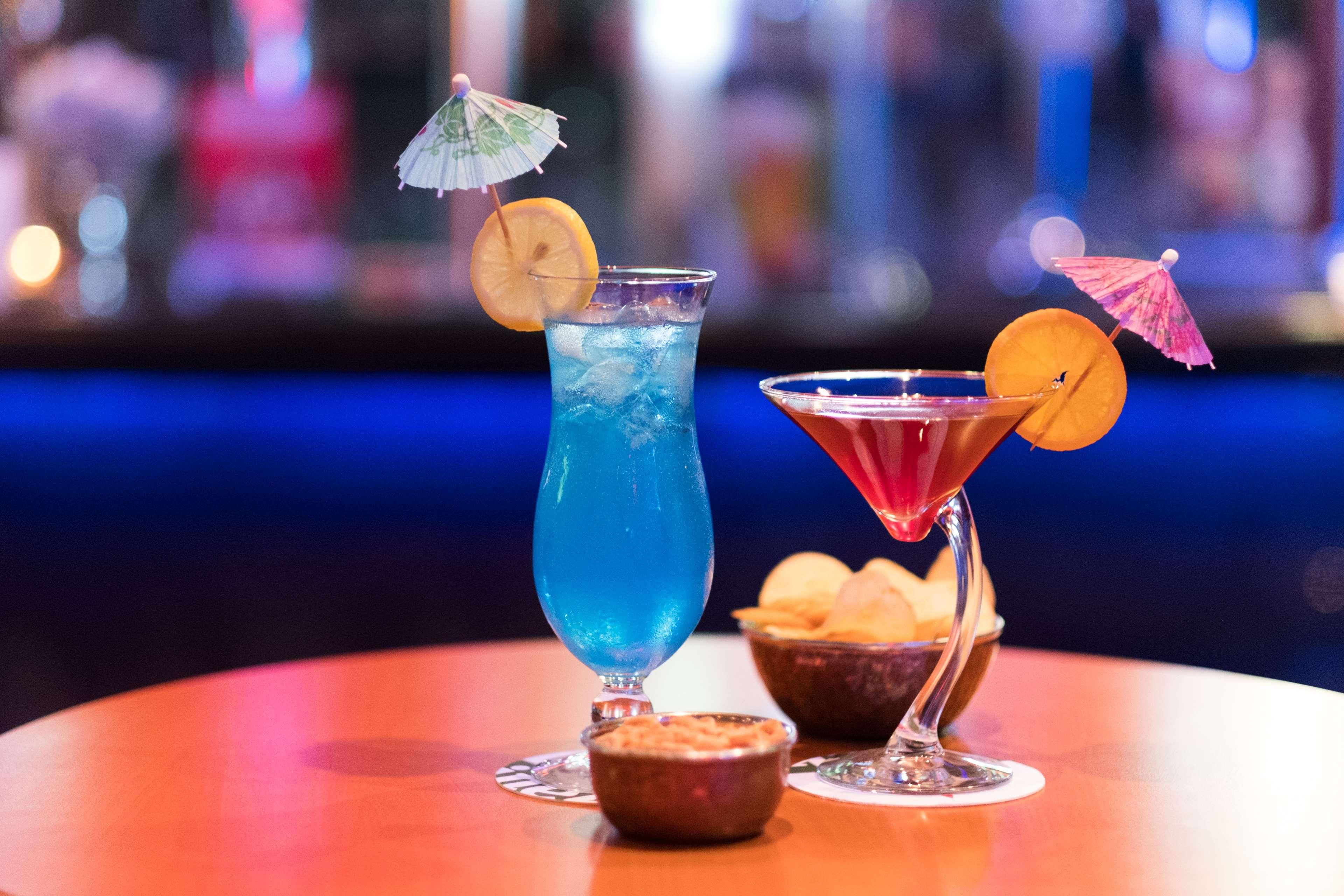 A bar setting with two drinks, one in a tall glass and one in a martini glass, both garnished with an umbrella and a slice of orange.