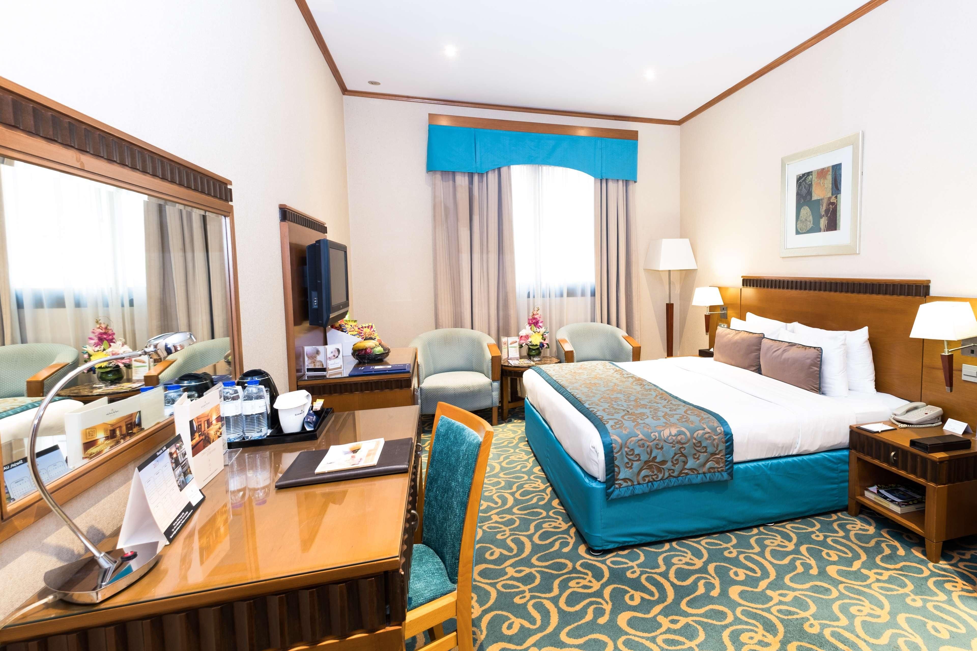 Habitación de hotel con cama, escritorio, sillas, televisor y ventana con cortinas.