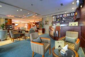 Eine Hotelhalle mit Sitzbereichen, einem Empfangstresen und einer Wand mit verschiedenen Ausstellungsstücken.