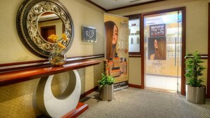 A reception area with a mirror, a sign for 'ROY,' a poster for 'nashi,' and two potted plants.