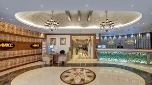 A hotel lobby with a reception desk, a large decorative floor pattern, and a chandelier.