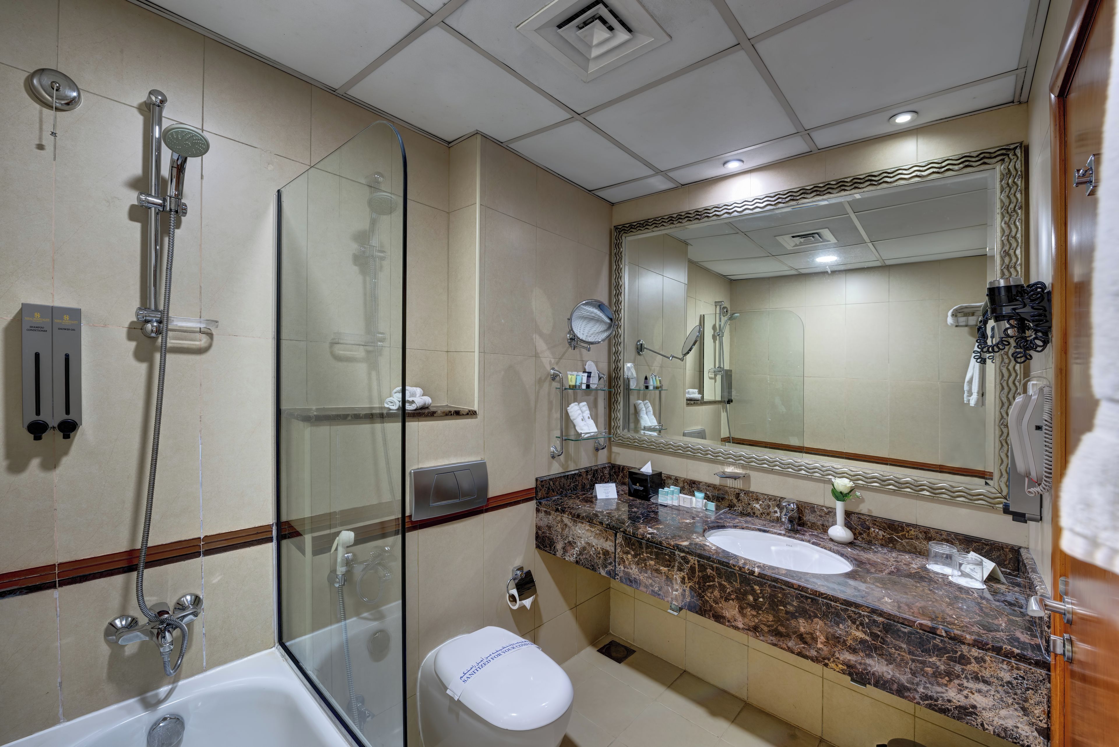 A modern bathroom with a glass-enclosed shower, a white toilet, a marble sink, and a large mirror.