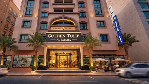 The exterior of the Golden Tulip Al Barsha hotel with a modern facade, palm trees, and a visible entrance.
