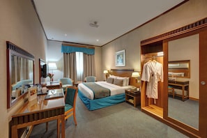 Ein Hotelzimmer mit Bett, Schreibtisch, Stuhl, Bademantelständer und Spiegel.