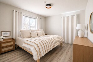Una camera da letto con un letto, comodini, una cassettiera, uno specchio e una finestra con tende.