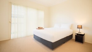A hotel room with a bed, a nightstand, a lamp, and a window with blinds. - Loftberg Villas (Muswellbrook)