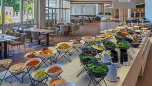 A buffet with various food stations and tables arranged in a spacious room with large windows.