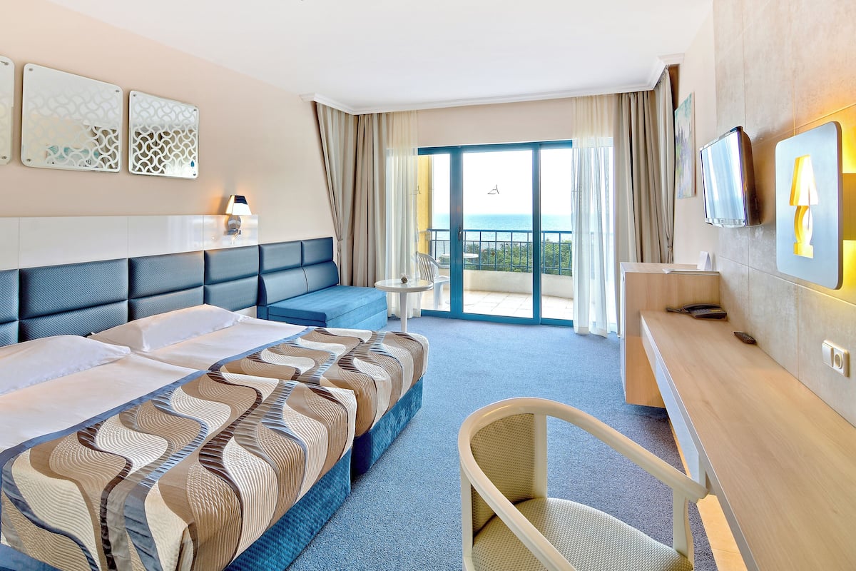 Ein Hotelzimmer mit einem großen Bett, einem Schreibtisch, einem Sessel und einem Balkon mit Meerblick.