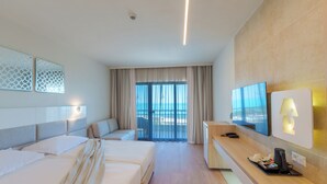A hotel room with two beds, a TV, a desk with a lamp, a coffee maker, and a view of the sea.