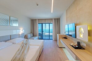 A hotel room with two beds, a TV, a desk with a lamp, a coffee maker, and a view of the sea. - Grifid Hotel Arabella (Varna)