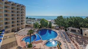 A hotel with multiple swimming pools, a view of the sea, and a large building with balconies.