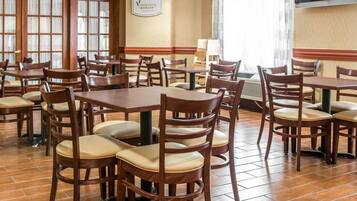 A hotel dining area with wooden tables and chairs, a large window with curtains, and a sign on the wall.