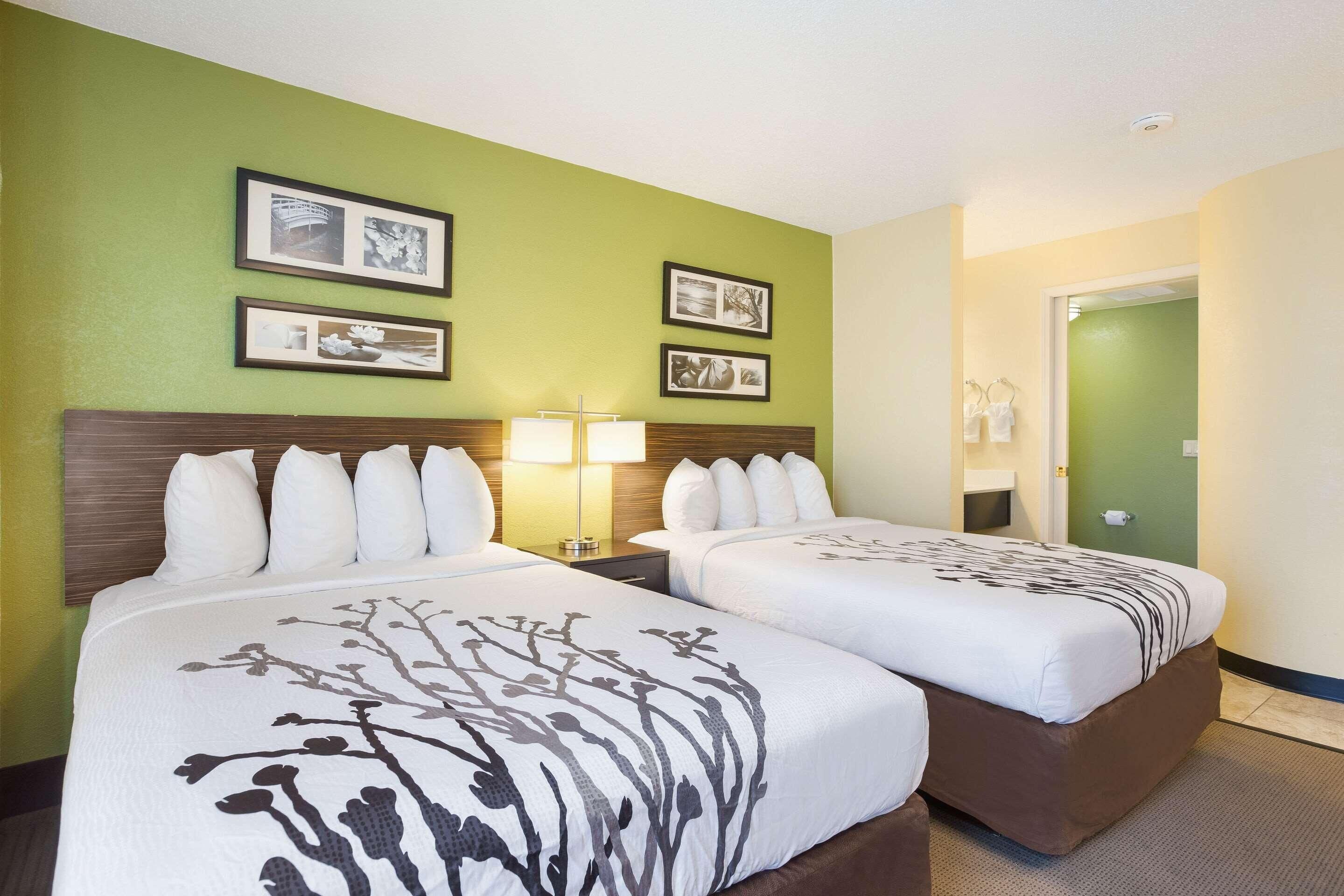 A hotel room with two beds, a nightstand with a lamp, and framed pictures on the wall.