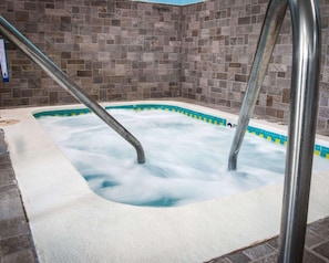 A hot tub with metal ladders, surrounded by stone walls. - Sleep Inn & Suites (Grand Rapids)