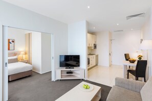 A modern hotel room with a bed, TV, dining area, and kitchenette. - Oaks Melbourne Lonsdale Suites (Melbourne)