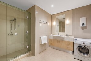 A modern bathroom with a glass-enclosed shower, a sink with a mirror, a towel rack, and a built-in washing machine. - Oaks Melbourne Lonsdale Suites (Melbourne)