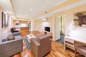 A modern living room with a sofa, TV, and a desk. - Oaks Melbourne Lonsdale Suites (Melbourne)