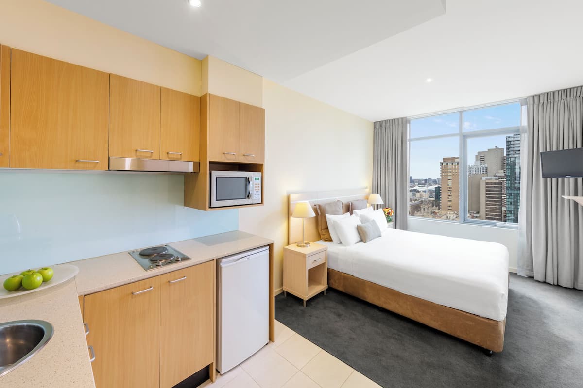 Habitación de hotel con cama, pequeña kitchenette, ventana con vista a la ciudad y televisión de pantalla plana.