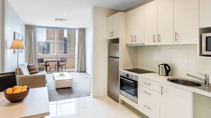 A modern hotel room with a balcony, a kitchenette, and a seating area with a sofa and coffee table. - Oaks Melbourne Lonsdale Suites (Melbourne)