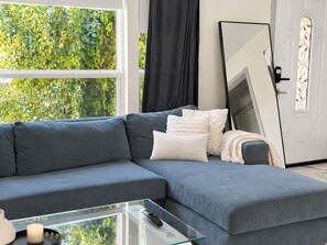 Ein modernes Wohnzimmer mit einem grauen Ecksofa, einem Glastisch und einem großen Spiegel.