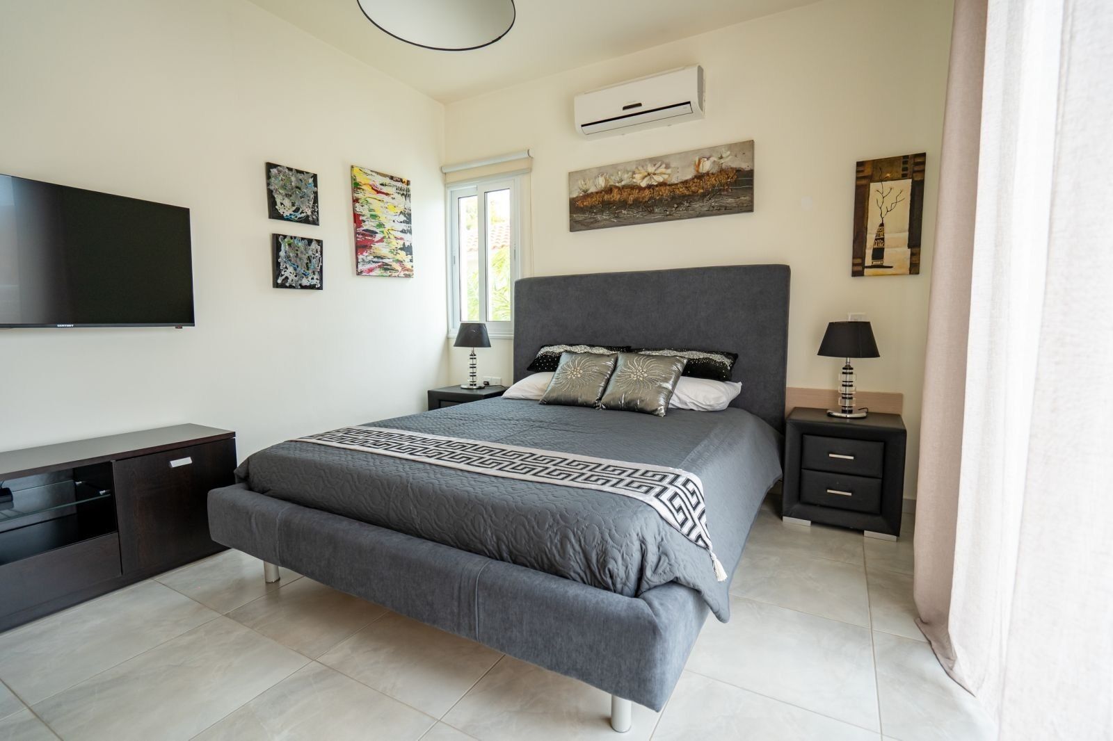 A modern bedroom with a large bed, a flat-screen TV, a desk, and artwork on the walls.