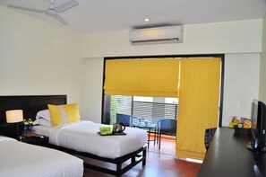 Ein Hotelzimmer mit Bett, Nachttisch, Lampe, Klimaanlage und einem Balkon mit gelben Vorhängen.