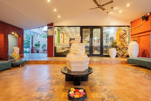 A reception area with a Buddha statue, a large potted plant, a bookshelf, and a seating area.